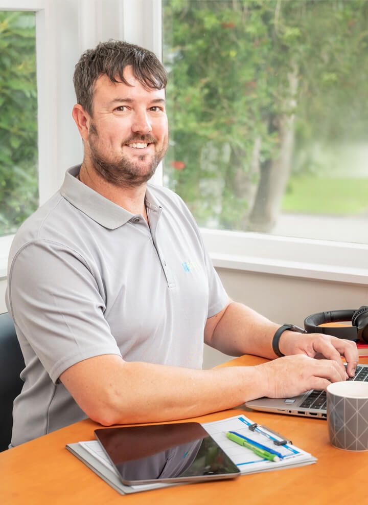 IT Squad Regan Scarfe sitting at desk on his laptop